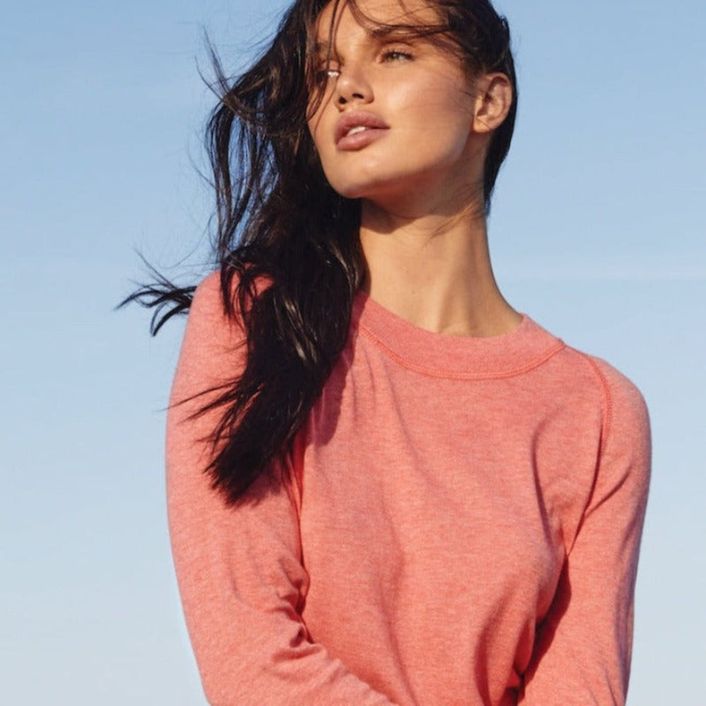 This image embraces natural motion with relaxed style, featuring a woman wearing our pastel red organic cotton RESTORE crewneck, crafted with of fine yarn with a smooth jersey  stitch