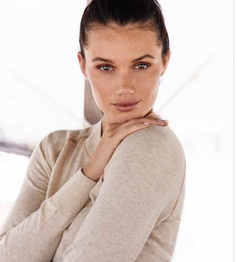 A woman is shown wearing the Restore Cotton Crewneck in a calm pose, embracing the supremely soft feel of the sweater's yarn and a sense of inner relaxation. The Restore sweater is so soft, you'll be tempted to sleep in it. The color shown in this photo is Lynx, a toasty beige neutral tone.