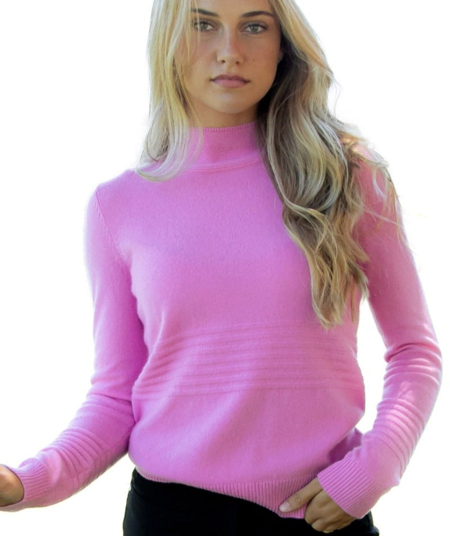 This photo shows a woman wearing the Isabella Carnation Pink Luxury Cashmere High Neck Golf Sweater, featuring sporty rib accents and intricate rib collar. Elegant and Sporty, the Isabella Cashmere Golf Sweater brings endless layering versatility to your everyday sustainable luxury wardrobe. Crafted in 2/28, 12GG Pure Cashmere