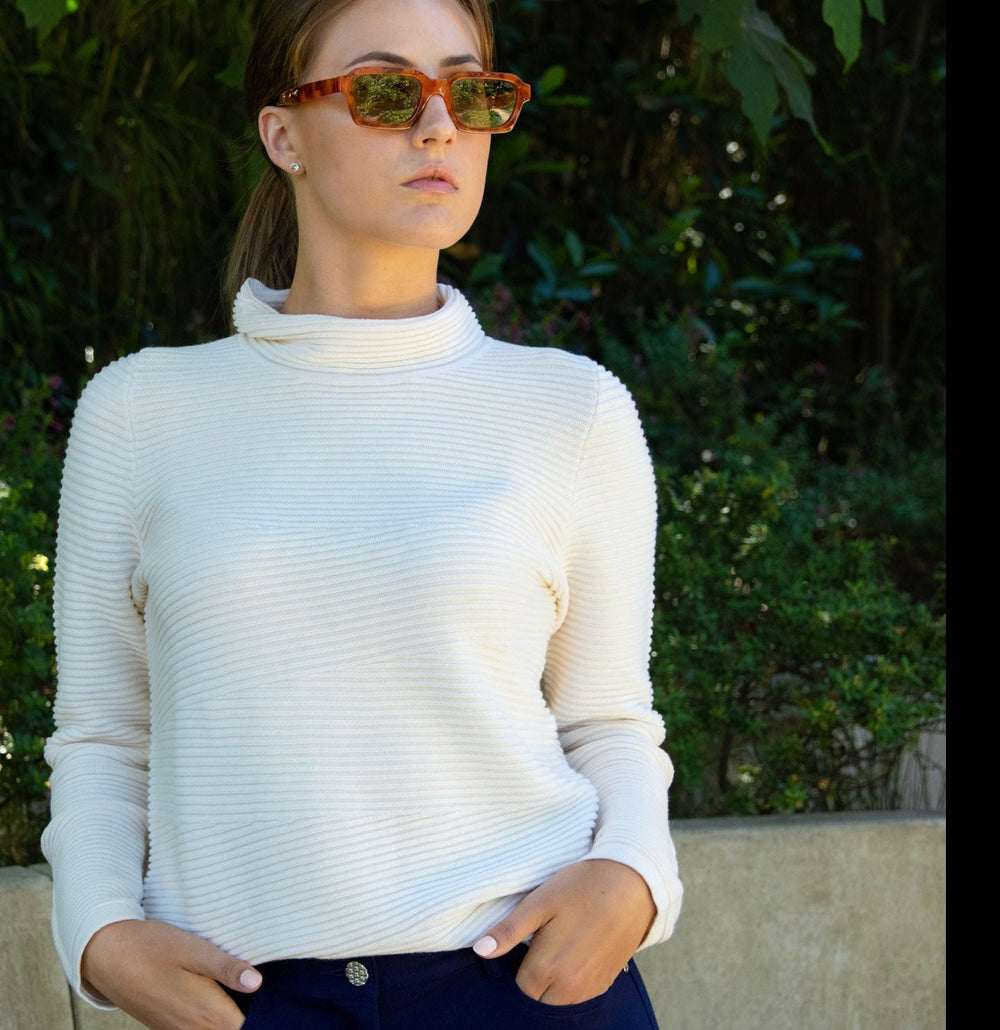 A sporty sweater with an elevated touch personifies everyday sophisticated and relaxed style that's versatile enough to wear for work-to-weekend travel. Sustainably crafted of Pure Cotton. This image shows a woman wearing the Ellie Cotton Link Funnel Neck Pullover in Natural Ivory, paired with the Navy 5-Pocket Stretch Jersey Eliza Pant.
