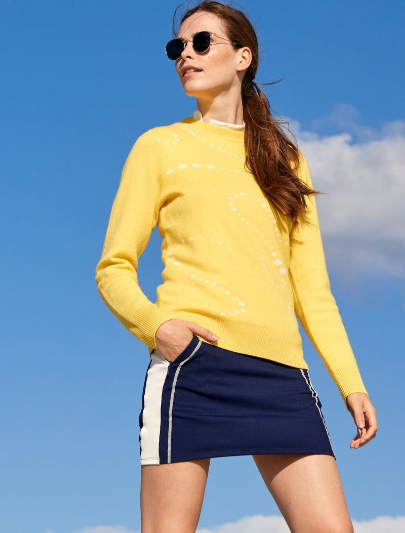 This image embraces elegant confidence and sporty style. The model is dressed in our Impact Performance Jersey Skort, Navy, size XS, paired with the Aubrey Sweater in Goldfinch, Yellow, crafted of Extra Fine Merino Wool and Cashmere. The sweater is layered over the Brooke top. A versatile and stylish combo that's as comfortable as it is chic.