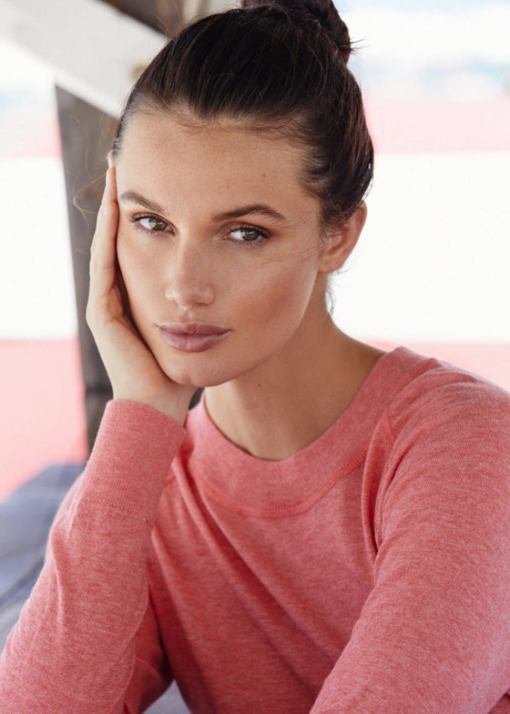 This image is a close-up view of a woman wearing the pastel red organic cotton Restore Sweater. Understated and chic, this year-round light weight crewneck has a vintage -inspired feel and is crafted of delicately soft organic cotton and Repreve for a luxurious buttery soft finespun jersey.
